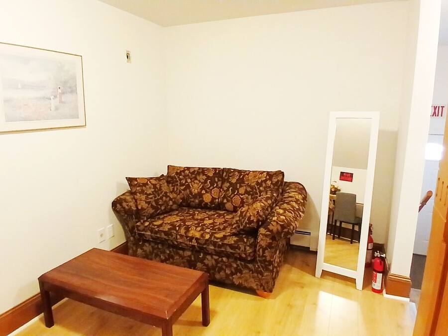 Una sala de estar con un sofá floral, una mesa de centro de madera, un cuadro enmarcado en la pared y una puerta que da a otra habitación.