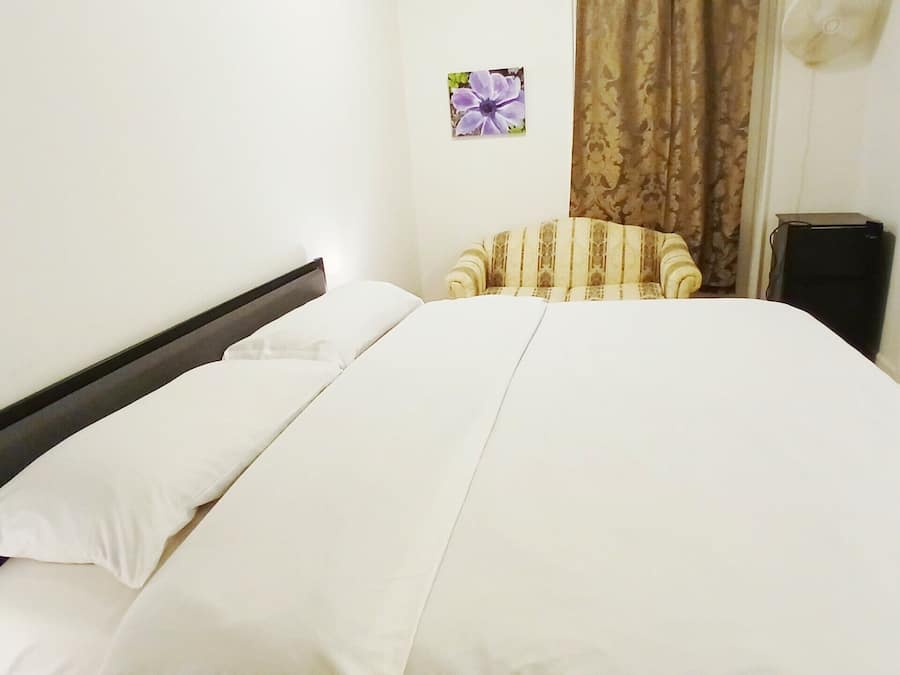 A bed with white linens, a wooden headboard, and a small decorative flower on the wall.