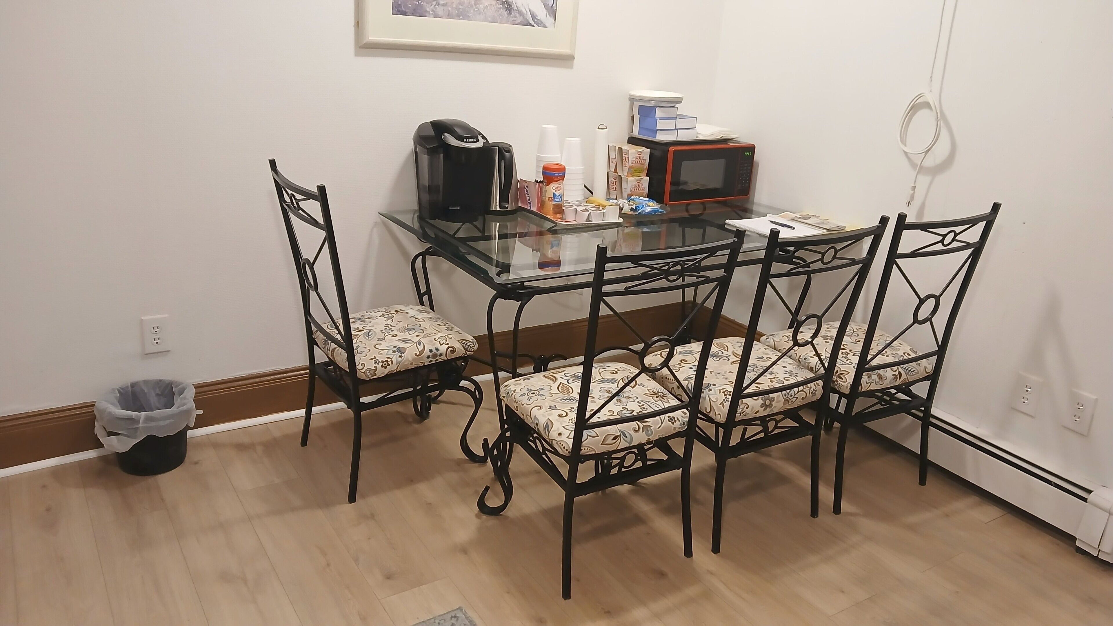 A small dining area with a glass table, four chairs, a coffee maker, and a microwave.