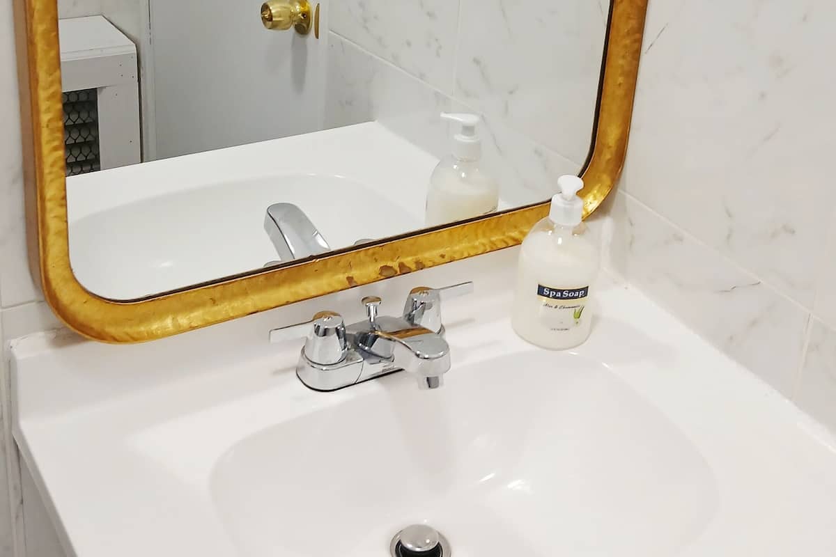 A bathroom with a white sink, a gold-framed mirror, and a bottle of spa soap.