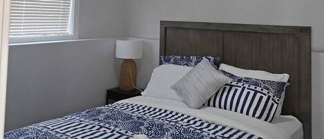 Een slaapkamer met een bed, nachtkastje, lamp en een raam met zonwering.