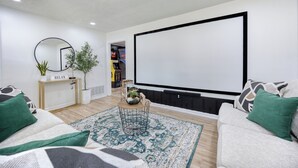 A living room with a large TV, a sofa, a coffee table, and a small side table with a plant. - Military in Style/Movie Room /Game Room Minutes from Ft. Benning & Downtown area (Columbus)
