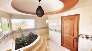 Un hall d’entrée spacieux avec un escalier en colimaçon, une porte en bois et un luminaire suspendu.