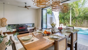 A dining area with a pool view, a television, and a ceiling fan. -  Bōld - Modern Tropical Pool Villas (Pecatu)