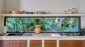 A kitchen with a large window, a sink, a vase with flowers, and a shelf with various items. -  Bōld - Modern Tropical Pool Villas (Pecatu)