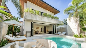 A modern outdoor pool area with lounge chairs, a built-in seating area, and lush greenery. -  Bōld - Modern Tropical Pool Villas (Pecatu)