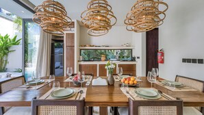 A dining area with a wooden table, wicker chairs, and a large fish tank in the background. -  Bōld - Modern Tropical Pool Villas (Pecatu)