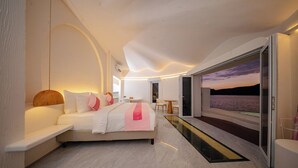 Une chambre moderne avec un grand lit, une table de chevet, une chaise et une vue sur la mer par une porte vitrée.