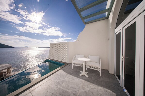 A balcony with a pool, white furniture, and a view of the sea.