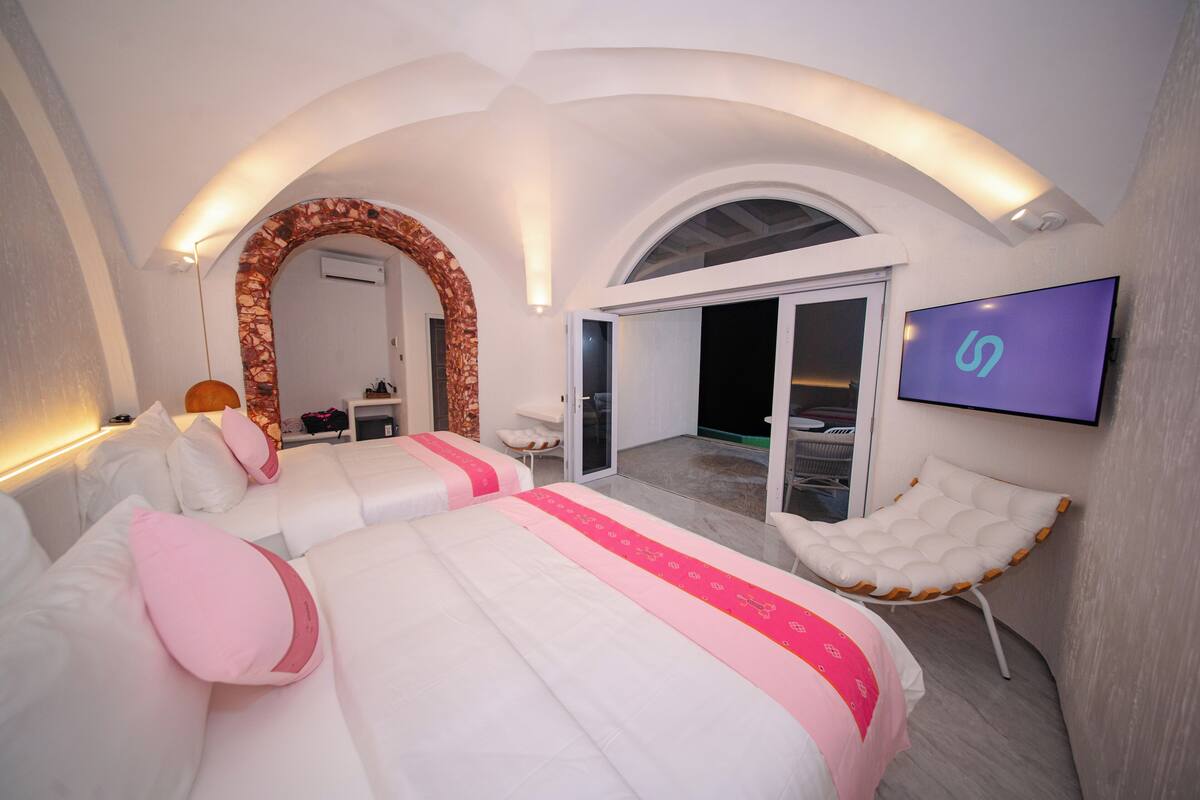 A modern hotel room with two beds, a TV, and a balcony.