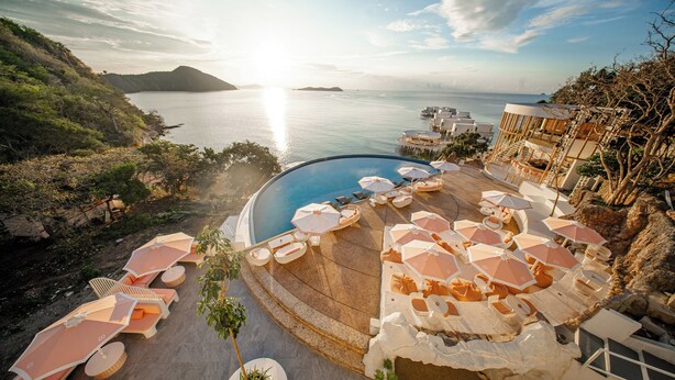 Un espace piscine aménagé dans un complexe hôtelier, avec des chaises longues et des parasols, offrant une vue sur une étendue d’eau et un paysage montagneux.