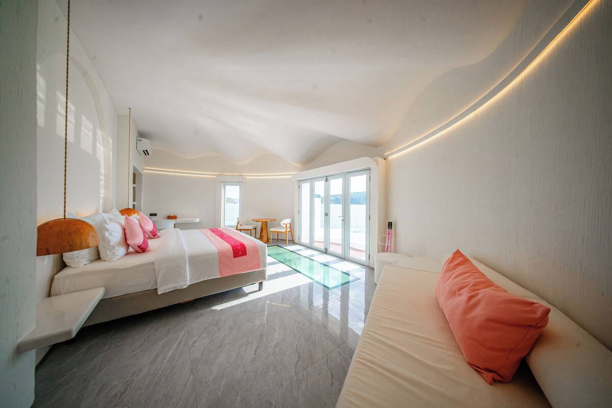 A modern bedroom with a bed, a sofa, a small table, and a view of the outdoors.