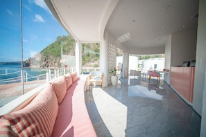 A modern interior with a curved ceiling, a seating area with a pink sofa, and a view of the sea and hills. - 69 Resort & Beach Club by Loccal Collection, Labuan Bajo (Labuan Bajo)