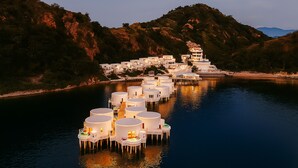 Une série de structures flottantes à plusieurs niveaux, reliées par des passerelles, situées sur une étendue d’eau calme, entourée de collines.
