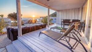 A wooden deck with a lounge chair and a table, overlooking a body of water and a sunset. - BUQEZ ECO RESORT - Villa 13 - Seafront (Drage)