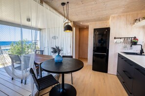 A modern kitchen with a black refrigerator, wooden cabinets, and a dining area with a round table and chairs. - BUQEZ ECO RESORT - Villa 13 - Seafront (Drage)