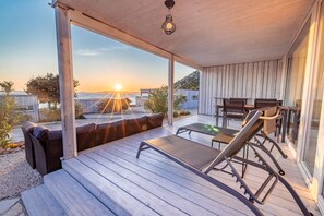 A wooden deck with a lounge chair and a table, overlooking a body of water and a sunset. - BUQEZ ECO RESORT - Villa 13 - Seafront (Drage)