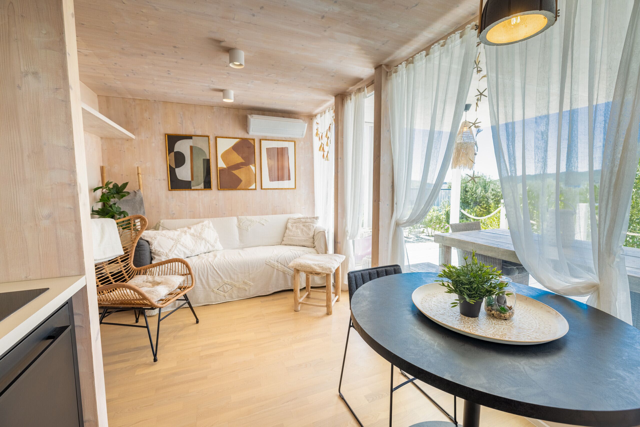 Een moderne woonkamer met een bank, stoelen, een eettafel met potplanten en uitzicht op groen.