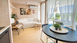 Una sala de estar moderna con un sofá, sillas, una mesa de comedor con plantas en macetas y vistas al verdor exterior.