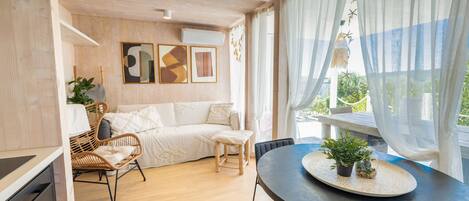 Een moderne woonkamer met een bank, stoelen, een eettafel met potplanten en uitzicht op groen.