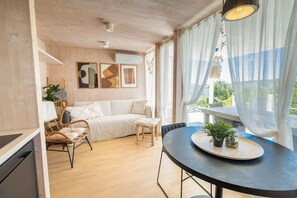 A modern living room with a sofa, chairs, a dining table with potted plants, and a view of greenery outside.