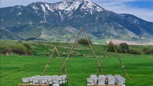 A grassy outdoor area with rows of chairs arranged for an event, set against a backdrop of snow-capped mountains. - Cottonwood cabin next to Pond (Swan Valley)