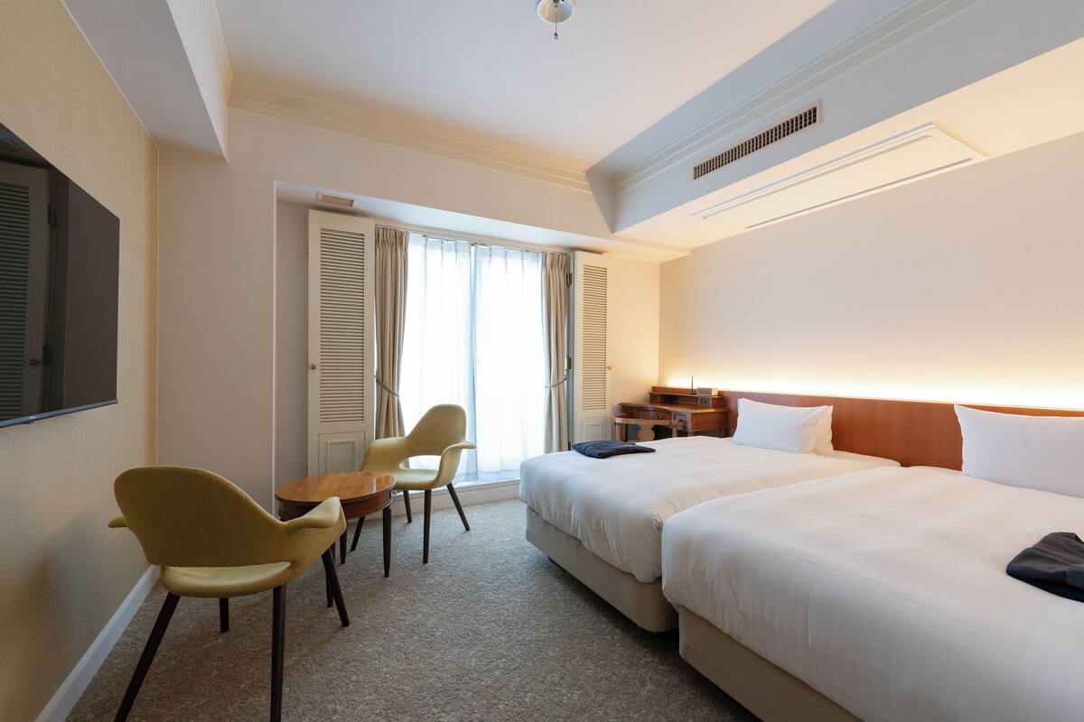 Ein Hotelzimmer mit zwei Betten, einem Schreibtisch, einem Stuhl und einem Fernseher.