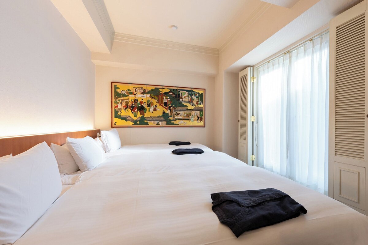 Una habitación de hotel con una cama grande, un cuadro en la pared y una ventana con persianas.