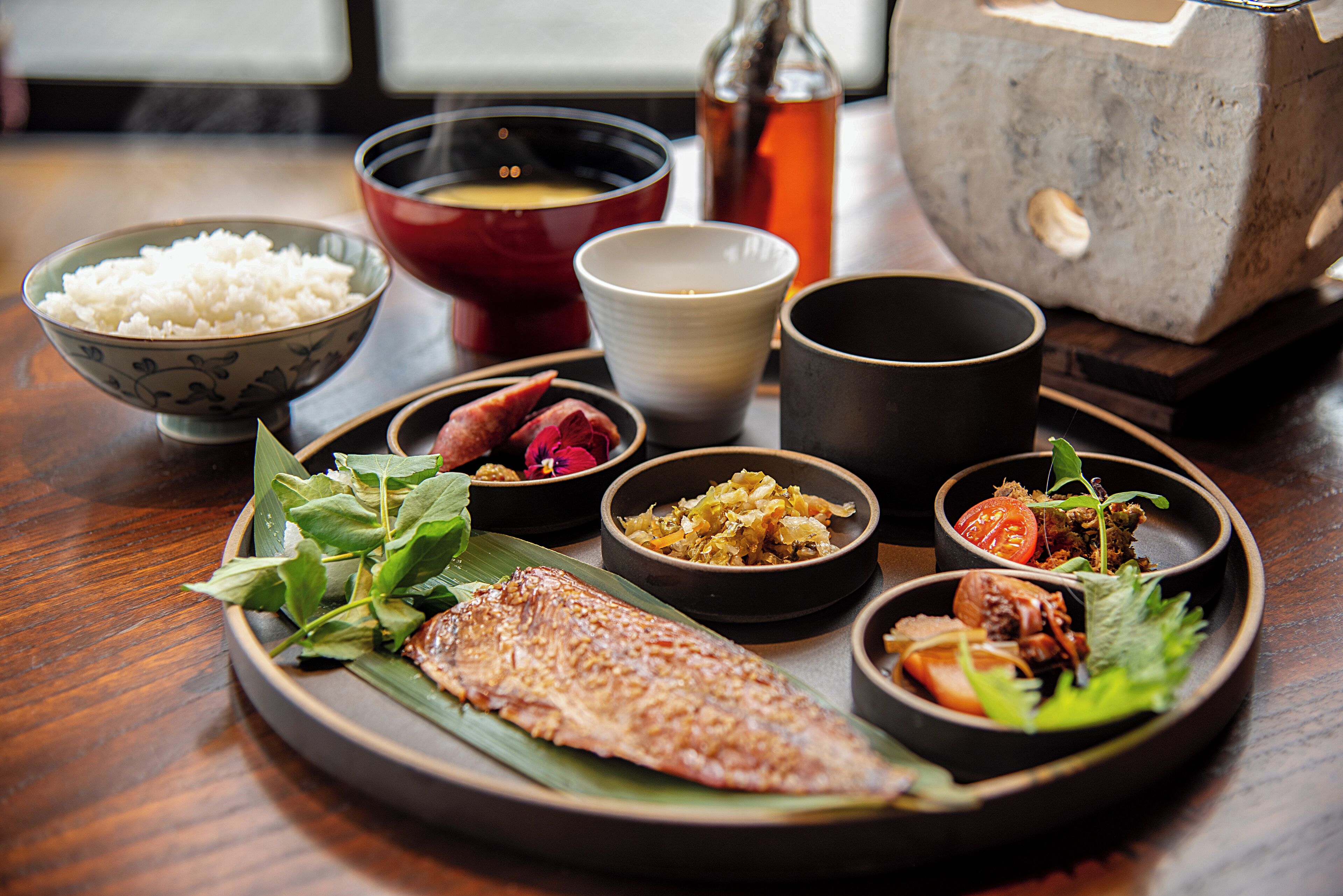 A traditional Japanese meal with rice, fish, and various side dishes on a wooden table.