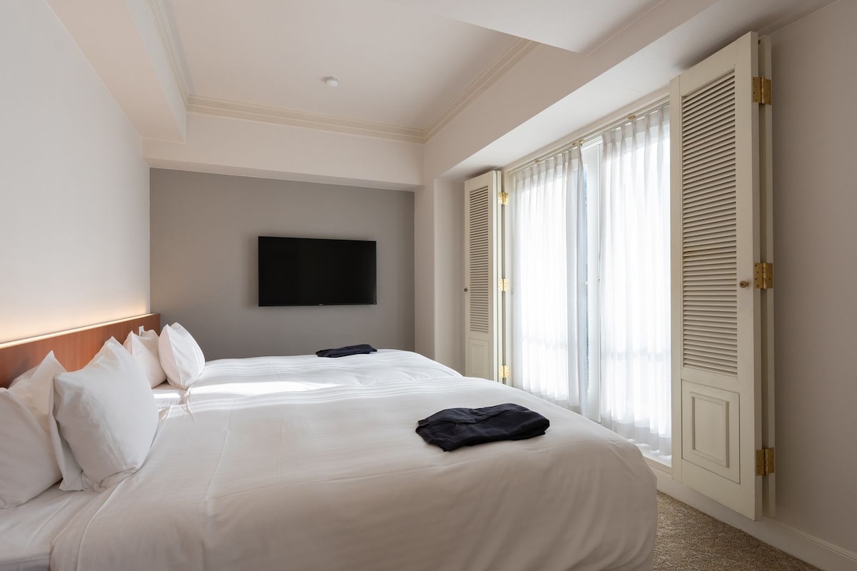 Habitación de hotel con una cama grande, un televisor de pantalla plana en la pared y una ventana con persianas.