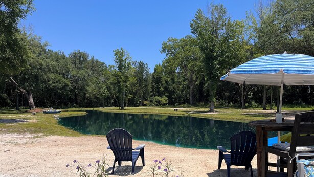 Una zona sabbiosa con due sedie Adirondack, una piccola barca e un tavolo con ombrellone.