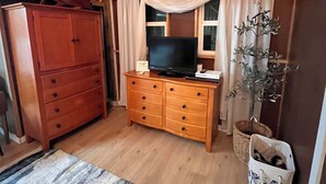 Una stanza con un comò in legno, una televisione sopra, una pianta e una finestra con tende.