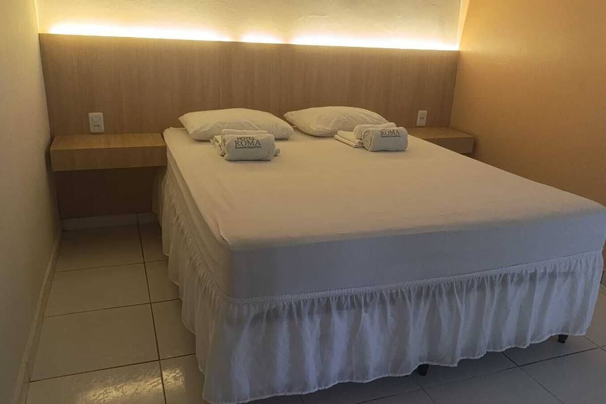 A hotel room with a bed, two pillows, a nightstand, and a wall-mounted light fixture.