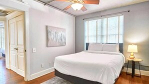A bedroom with a bed, a ceiling fan, a window with blinds, and a bedside lamp. - Terrific Dallas Location! 2BR w/ Wi-Fi & A/C – Knight 205 (Dallas)