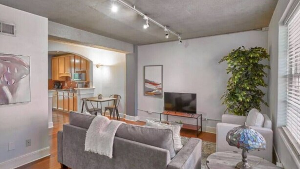 A modern living room with a grey sofa, a TV, and a dining area in the background. - Terrific Dallas Location! 2BR w/ Wi-Fi & A/C – Knight 205 (Dallas)