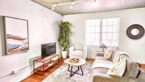 A modern living room with a flat-screen TV, a sofa, a coffee table, a potted plant, and a large window. - Terrific Dallas Location! 2BR w/ Wi-Fi & A/C – Knight 205 (Dallas)