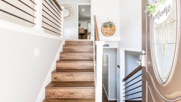 Una escalera de madera que lleva a una habitación con un letrero de 'Welcome' y un tapiz decorativo.