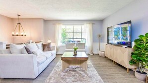 Una sala de estar moderna con un sofá blanco, una mesa de centro de madera y un televisor sobre un mueble.