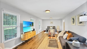 Ein geräumiges Wohnzimmer mit einem großen Flachbildfernseher, einem hölzernen Couchtisch, einem grauen Sofa und einem dunklen Sessel.