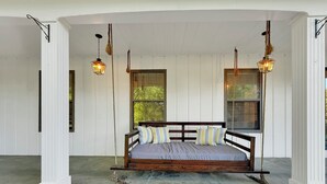 Ein hölzernes Bett mit gestreiften Kissen auf einer Veranda mit weißen Wänden und Fenstern.