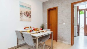 Un coin repas avec une table dressée pour deux personnes, un tableau accroché au mur et une porte en bois.