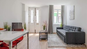 Un salon moderne avec un canapé gris, une table blanche et une petite table d’appoint sur laquelle est posée une plante.
