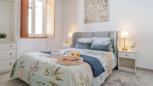 Un dormitorio con cama, mesitas de noche, una ventana y una obra de arte en la pared.