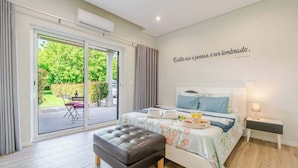 A modern bedroom with a large sliding glass door leading to a garden, a bed with a floral bedspread, and a bedside table with a lamp. - 10BR Douro Villa with Pool by HostWise (Santa Marinha do Zêzere)