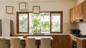 Una cocina moderna con armarios de madera, una isla central con taburetes de bar, un refrigerador, un microondas y vistas al exterior a zonas verdes.