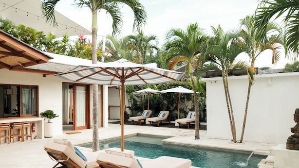 Zona de piscina con sillones, sombrillas y un bar.