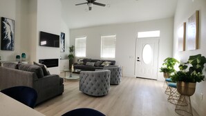 A spacious living room with a grey sofa, ottomans, a flat-screen TV, and a ceiling fan. - 3-bedroom house in Orlando near Universal Studios (Orlando)