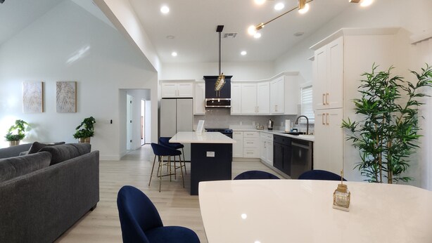 A modern kitchen with white cabinets, a central island, and a dining area with a white table and blue chairs. - 3-bedroom house in Orlando near Universal Studios (Orlando)