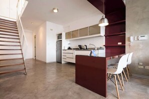 Une cuisine moderne avec un îlot central, des chaises blanches et un escalier.