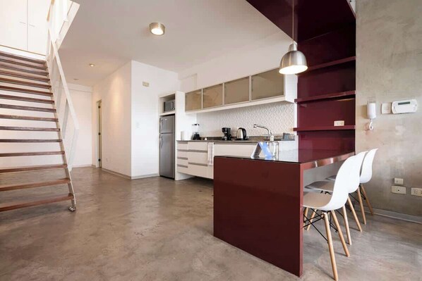 A modern kitchen with a central island, white chairs, and a staircase.